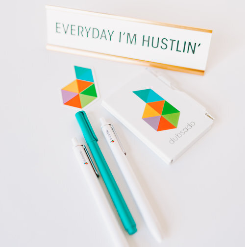 Desk placard that says "everyday I'm hustlin'" with Dubsado stickers and pens